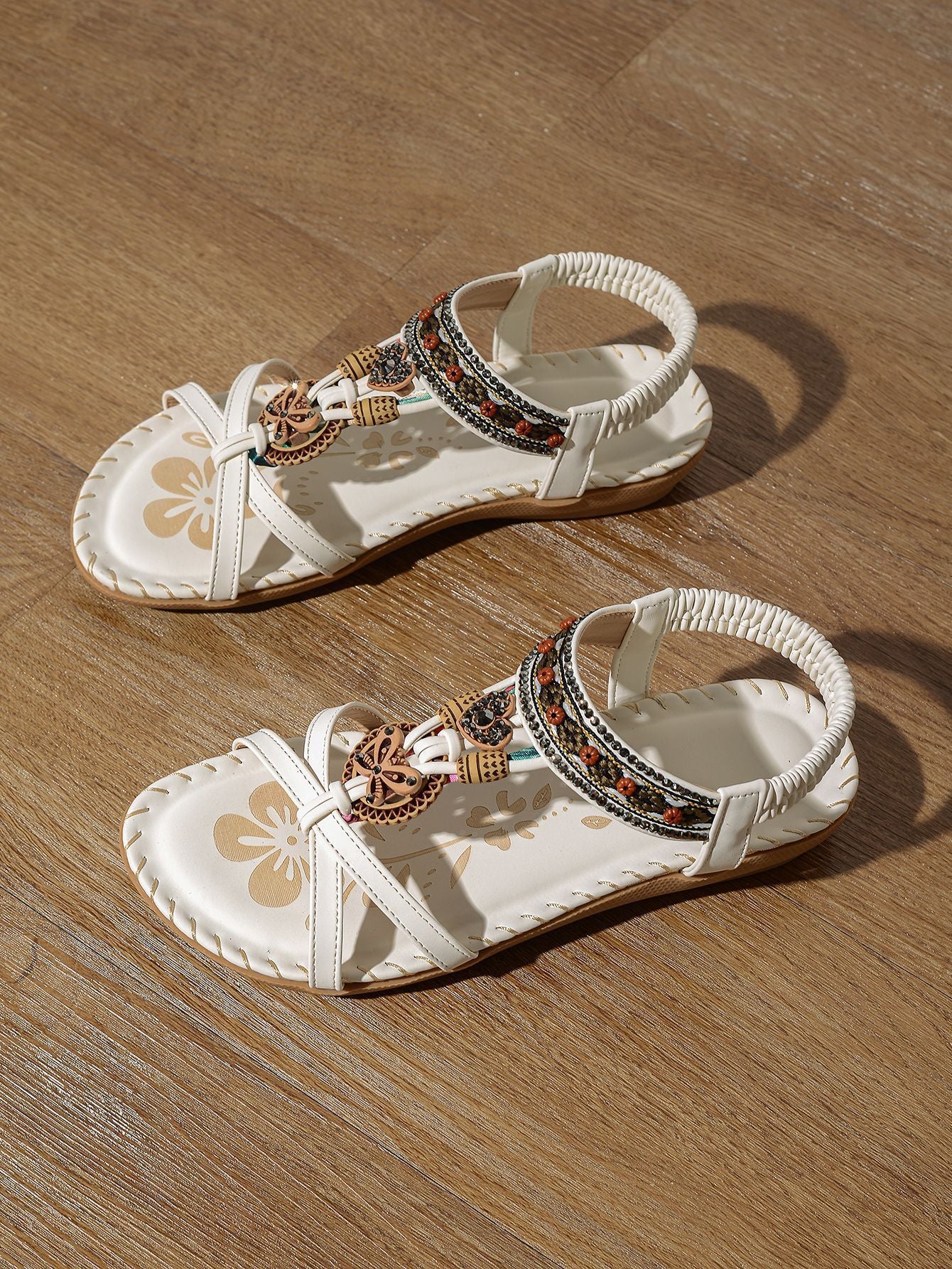 Pair of white sandals with decorative straps on a wooden surface