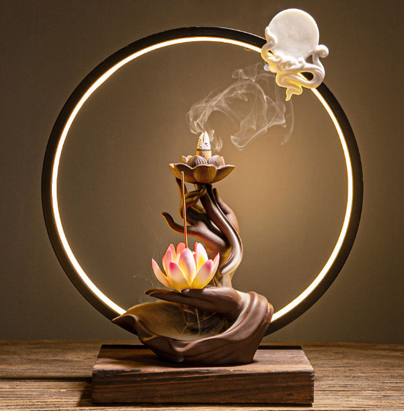 Decorative incense burner with lotus design on a wooden base, emitting smoke against a dark background.