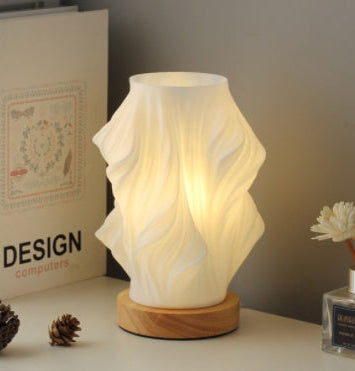 Decorative lamp with wavy design on a wooden base, placed on a surface with books and decorative items.