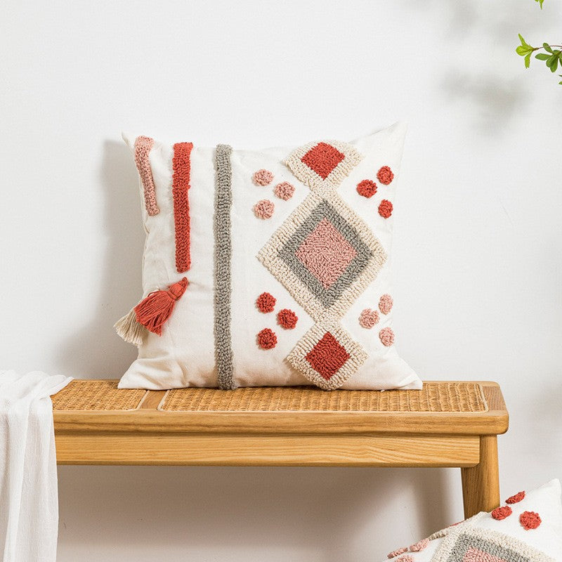 Decorative pillow with geometric pattern on a wooden bench against a white wall.
