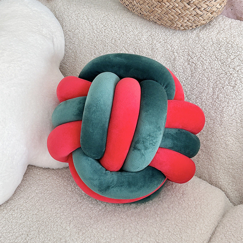 Decorative pillow with knot design in red and green on a soft surface