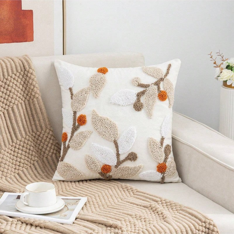 Decorative pillow with leaf pattern on a couch with a blanket and cup of coffee.