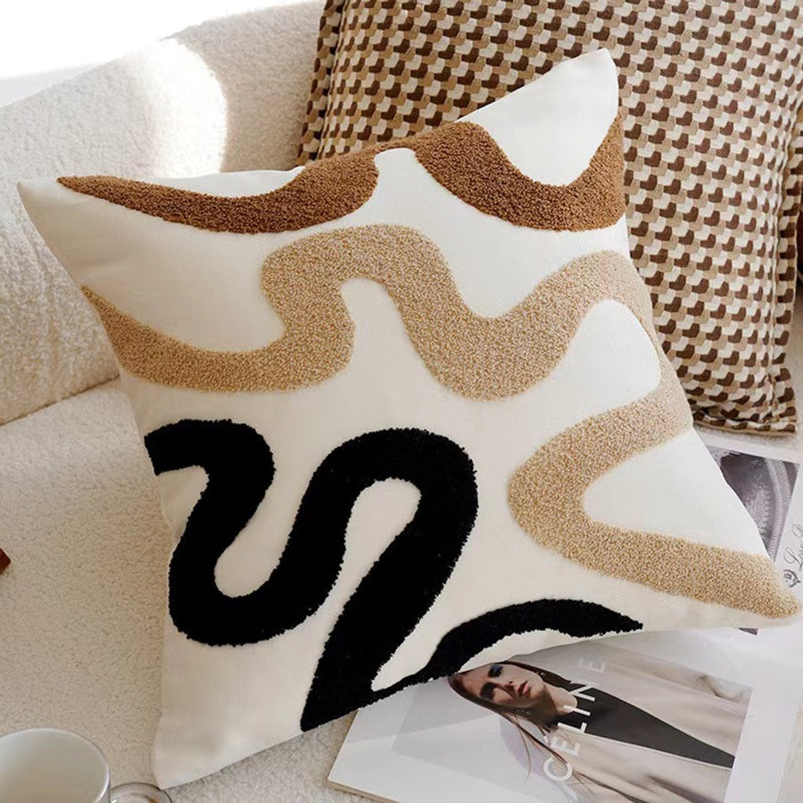Decorative pillow with wavy pattern and letter 'S' on a couch with a magazine and mug.
