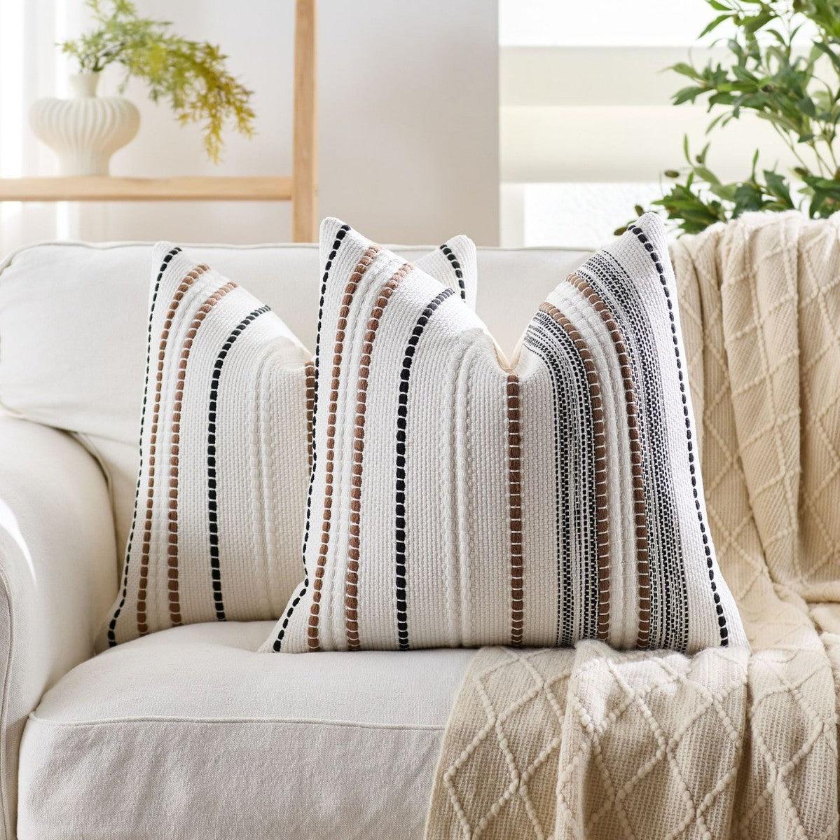 Decorative pillows with striped pattern on a white sofa in a bright living room.