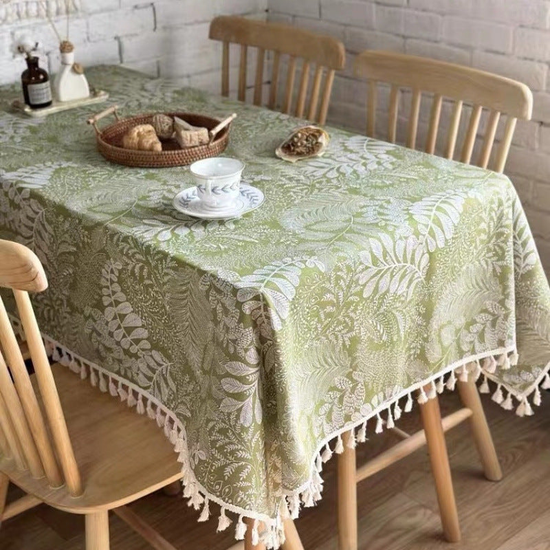 Dining table with a green floral tablecloth and wooden chairs.
