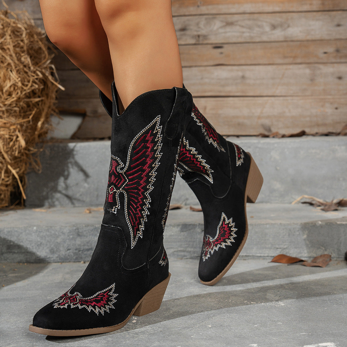 Black cowboy boots with red and white embroidery on a wooden background