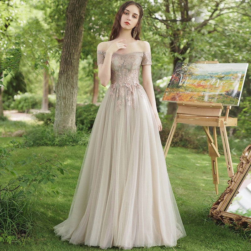Woman in a beige evening gown standing in a garden with a painting on an easel.