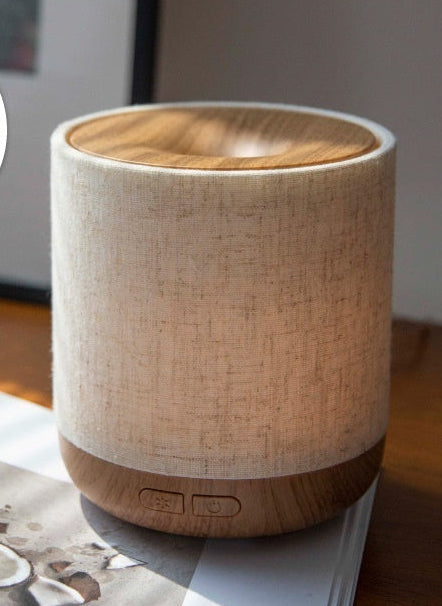 Fabric-covered diffuser with wood grain base on a surface with text describing features.