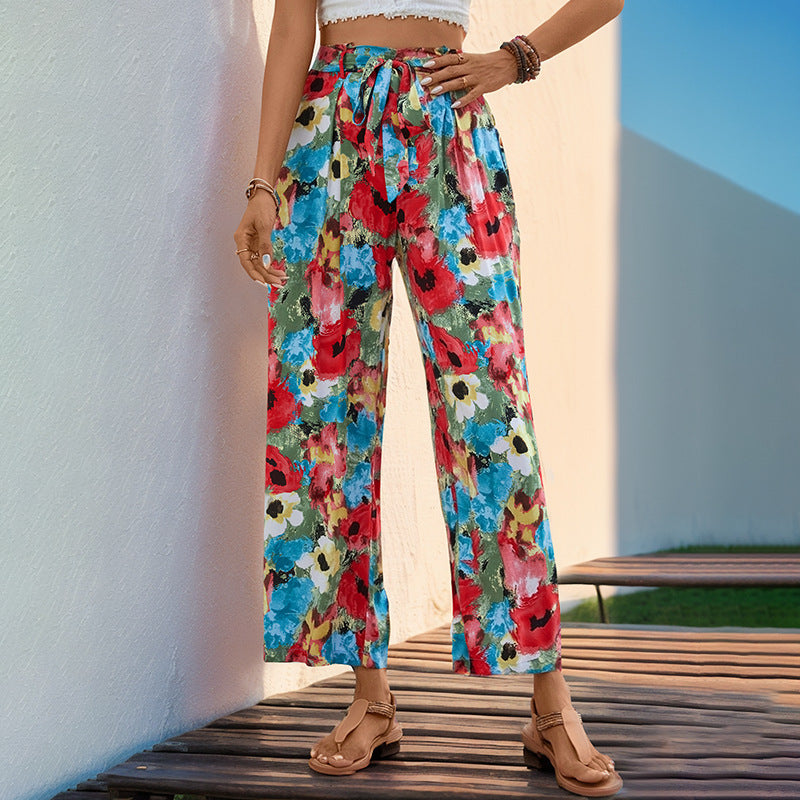 Person wearing colorful floral pants sitting on a wooden bench with a white wall and blue sky in the background.