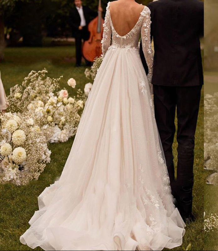 Person in a white wedding dress standing outdoors with floral arrangements and a musician in the background.