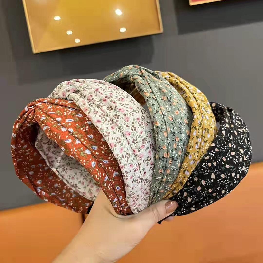Stack of floral-patterned headbands held by a hand against a neutral background