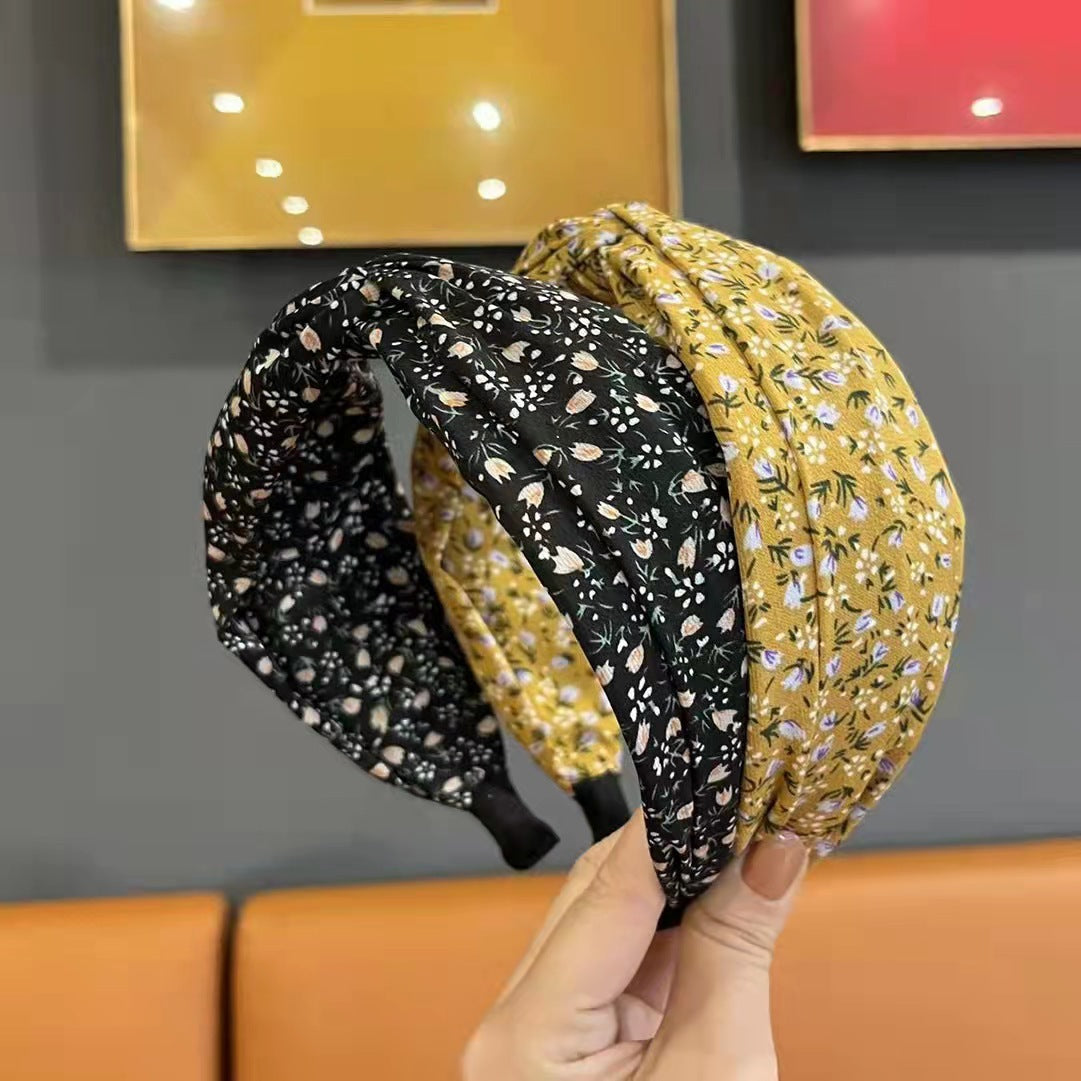 Two patterned headbands held by a hand against a gray wall with framed pictures.