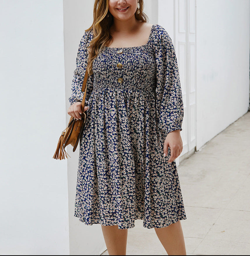 Woman wearing a floral dress standing against a white wall.