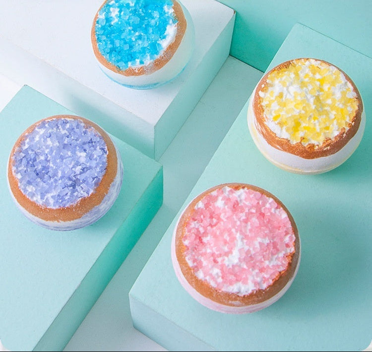 Four round bath bombs with colorful toppings on a light blue surface.