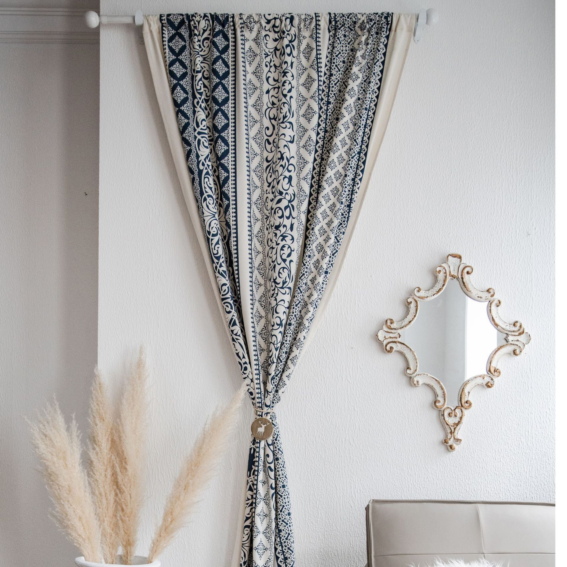 Decorative curtain with geometric pattern hanging on a white wall with a mirror and plant in the background.