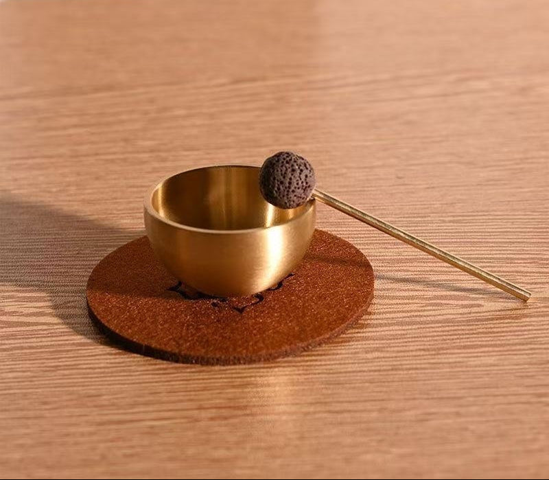Gold incense holder with a spherical incense cone on a wooden coaster, placed on a wooden surface.
