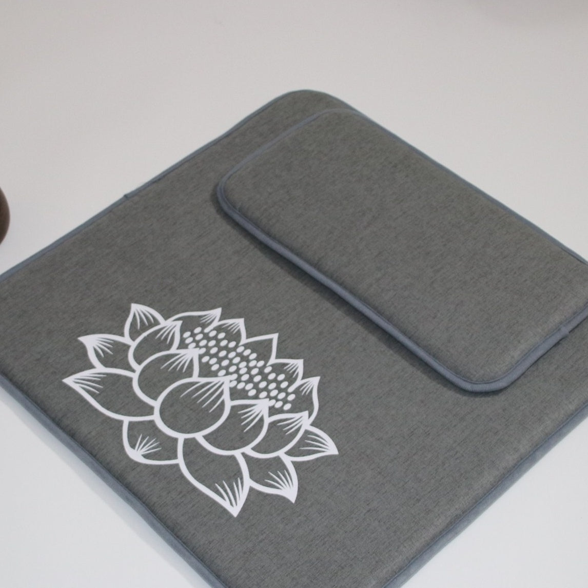 Gray laptop sleeve with white lotus flower design on a light gray background