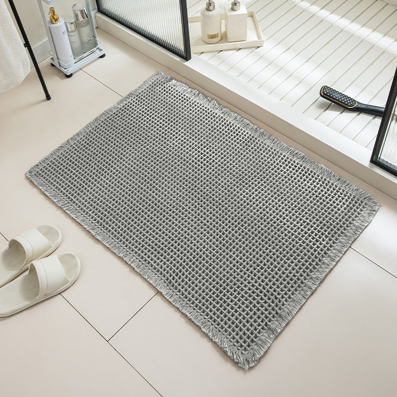 Gray textured bath mat on a tiled bathroom floor with white slippers and a remote control.
