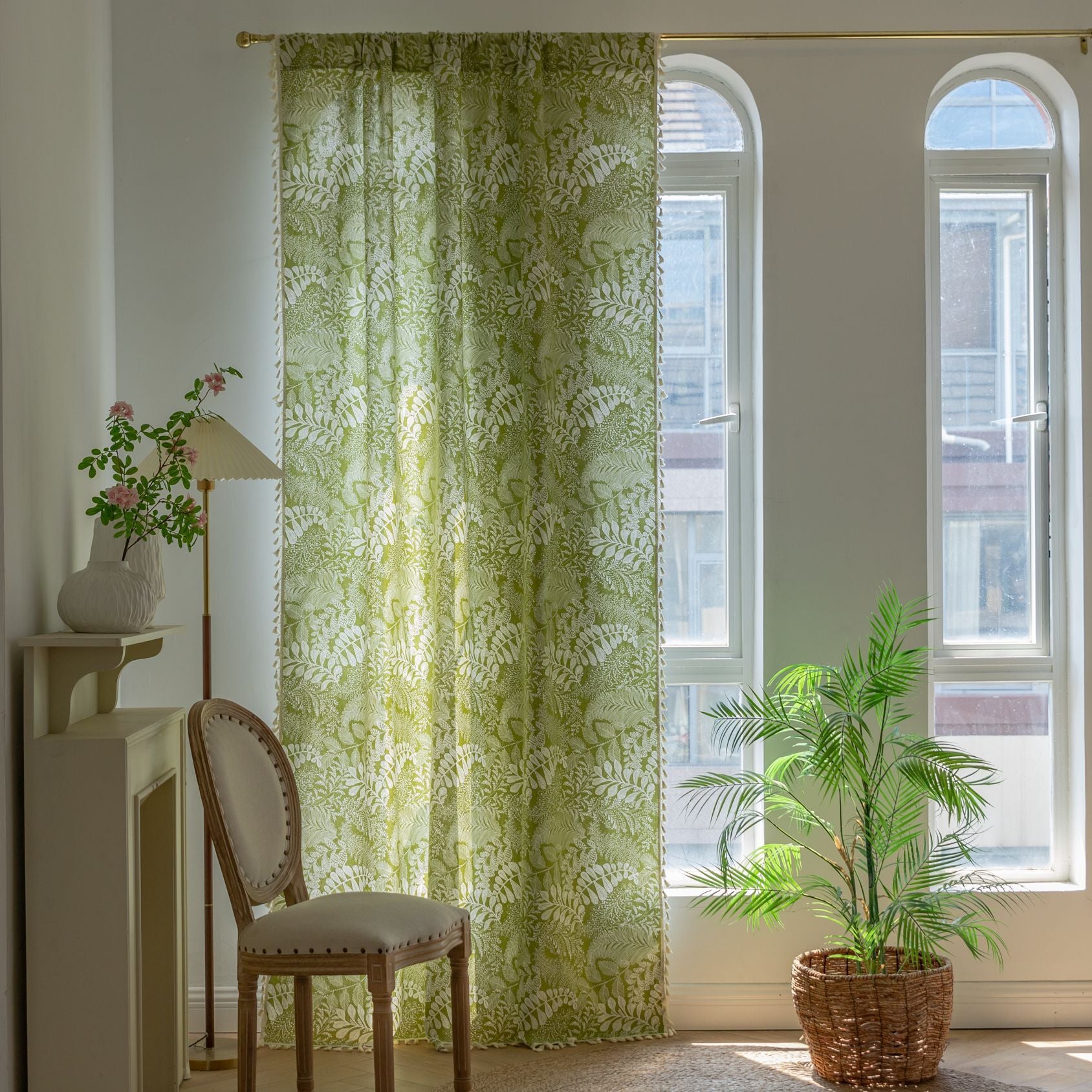 Room with green floral curtains, a chair, and a plant near a window.