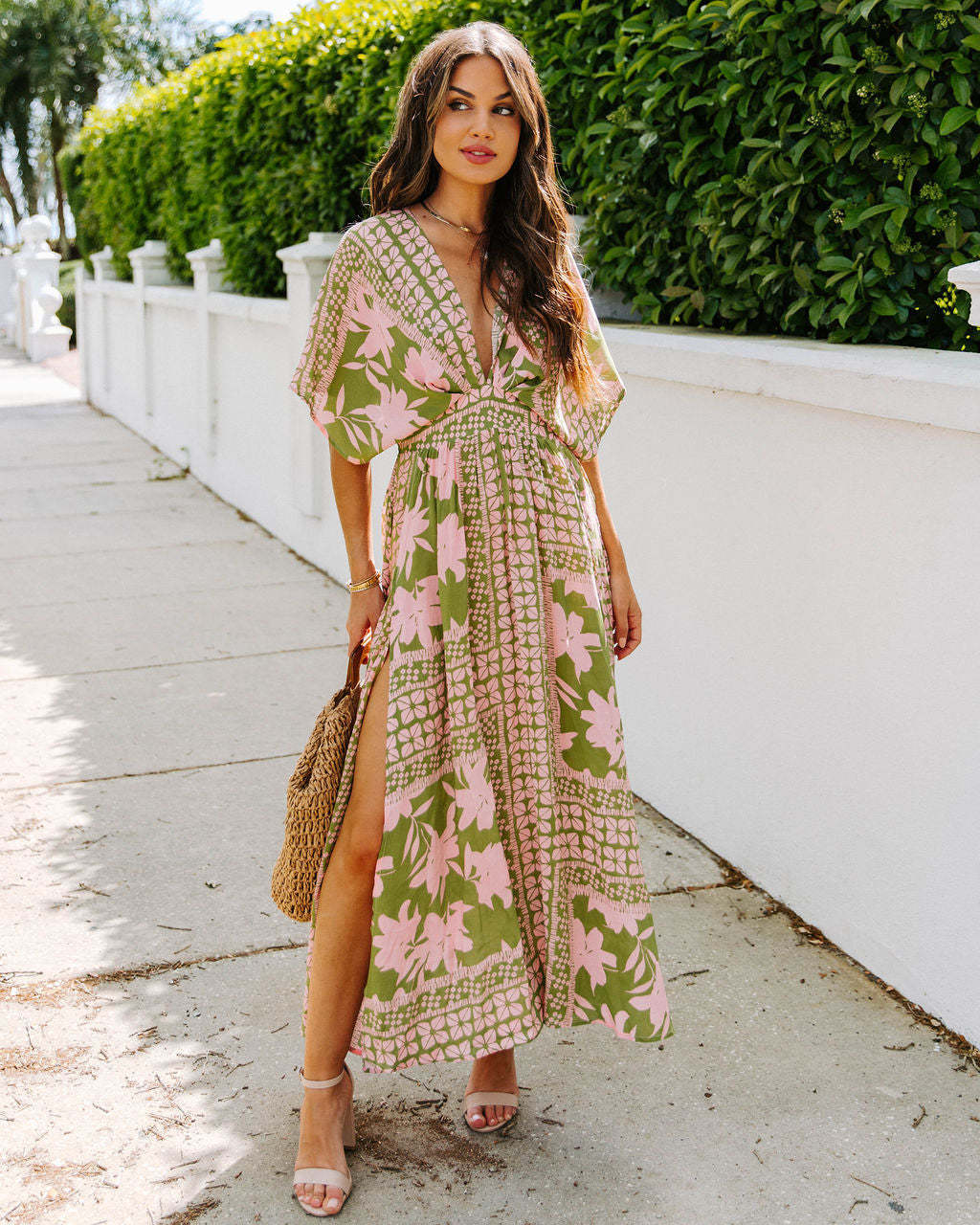 Woman wearing a floral dress with a white wall and greenery in the background