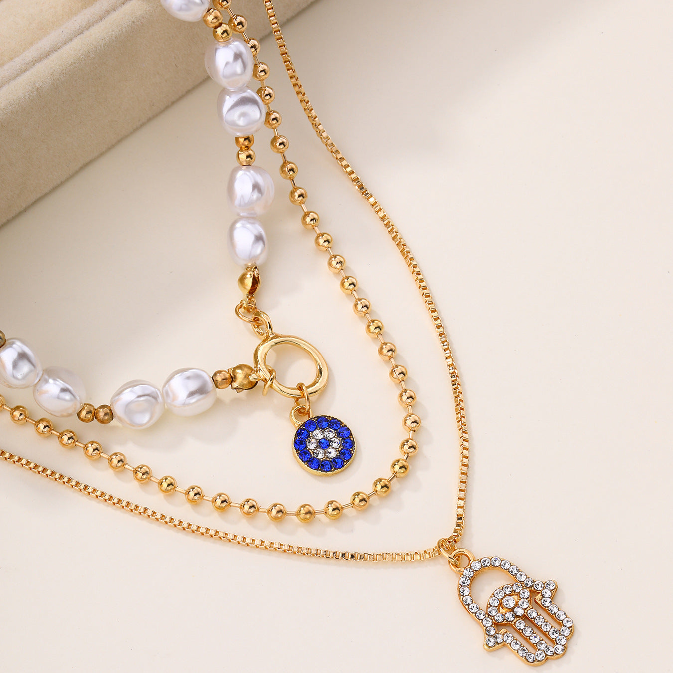 Gold necklace with pearl strands and hamsa hand charm on a beige background