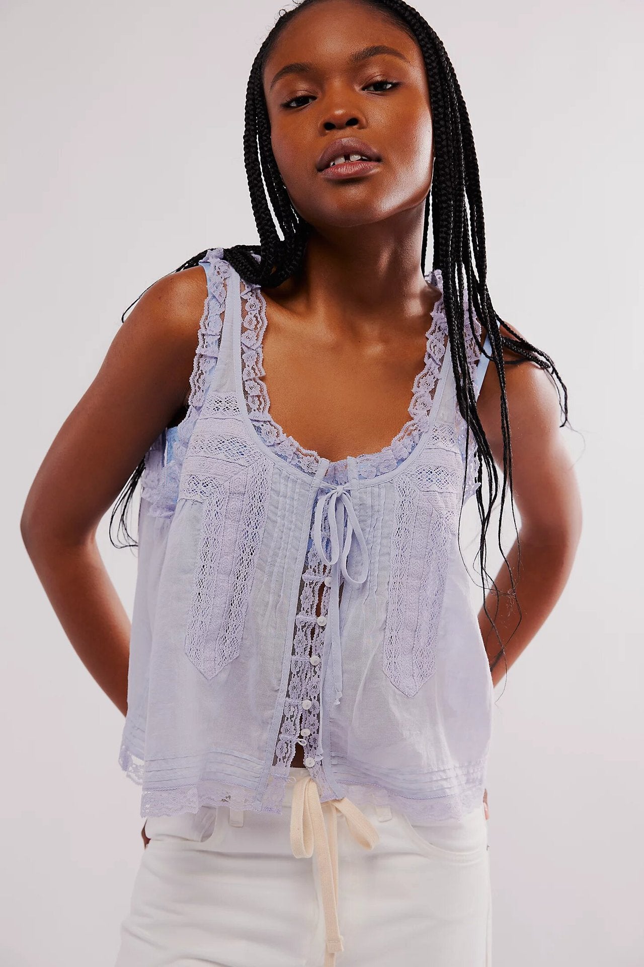 Woman wearing a light blue sleeveless top with lace details on a white background