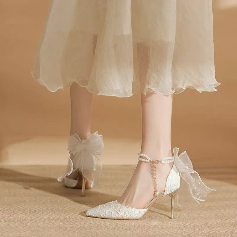 White lace high-heeled shoes with ribbons worn with a light-colored dress on a neutral background