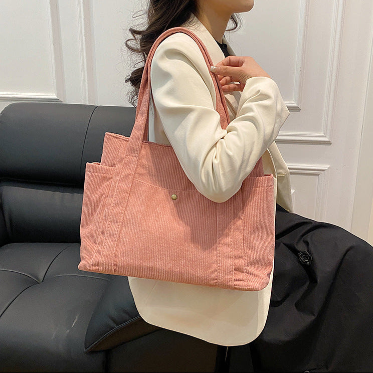 Person holding a pink tote bag in a room with a gray sofa.