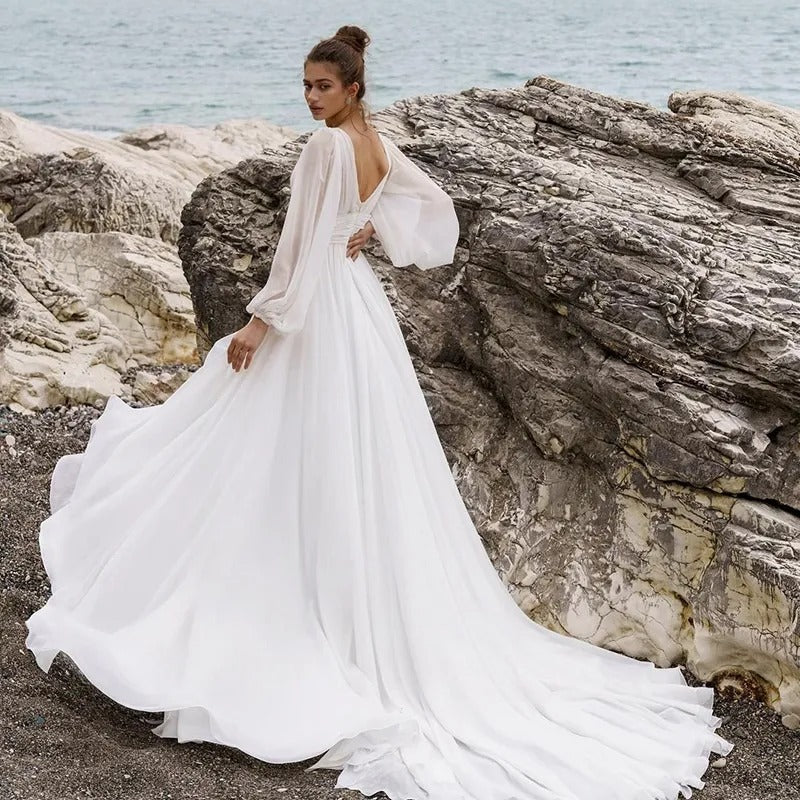 Woman in a white wedding dress standing on rocky terrain by the sea.