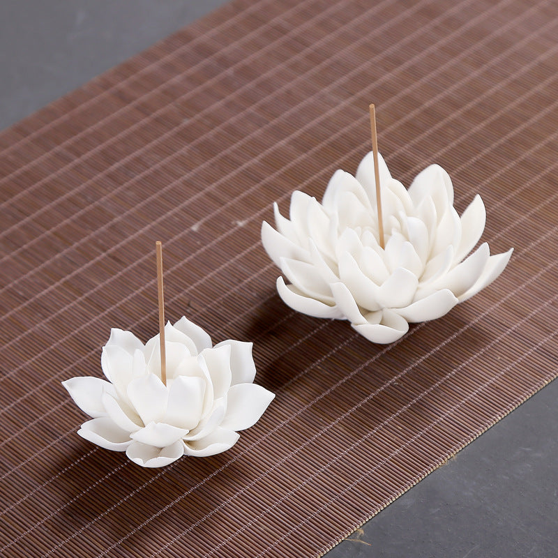 Two white ceramic lotus incense holders on a brown mat.