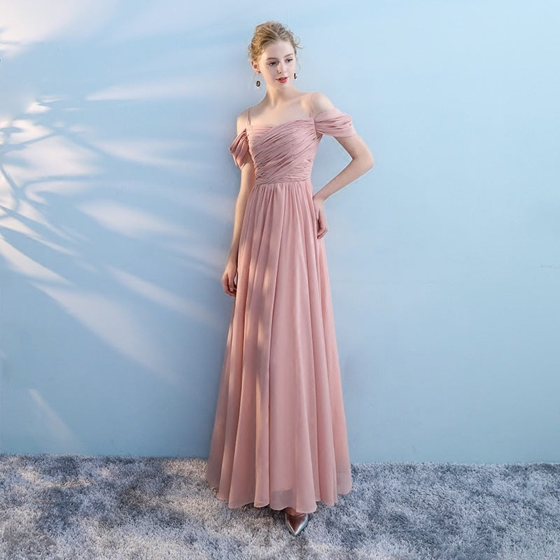Woman wearing a pink off-shoulder gown against a light blue wall.