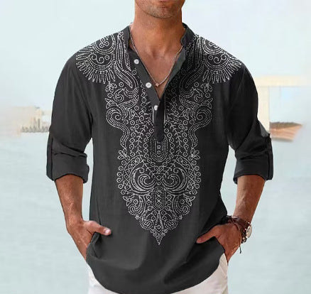 Man wearing a black embroidered shirt with white pants against a light blue background