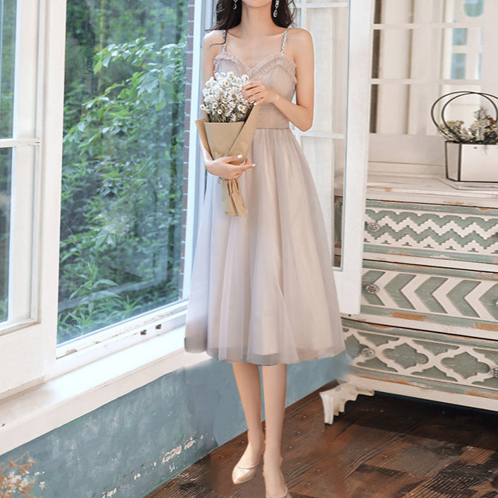 Woman in a beige dress holding flowers in a room with large windows and decorative elements.