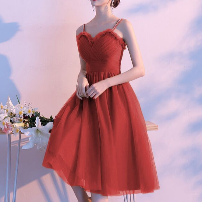 Woman in a red dress standing against a soft, blurred background with flowers on a table.