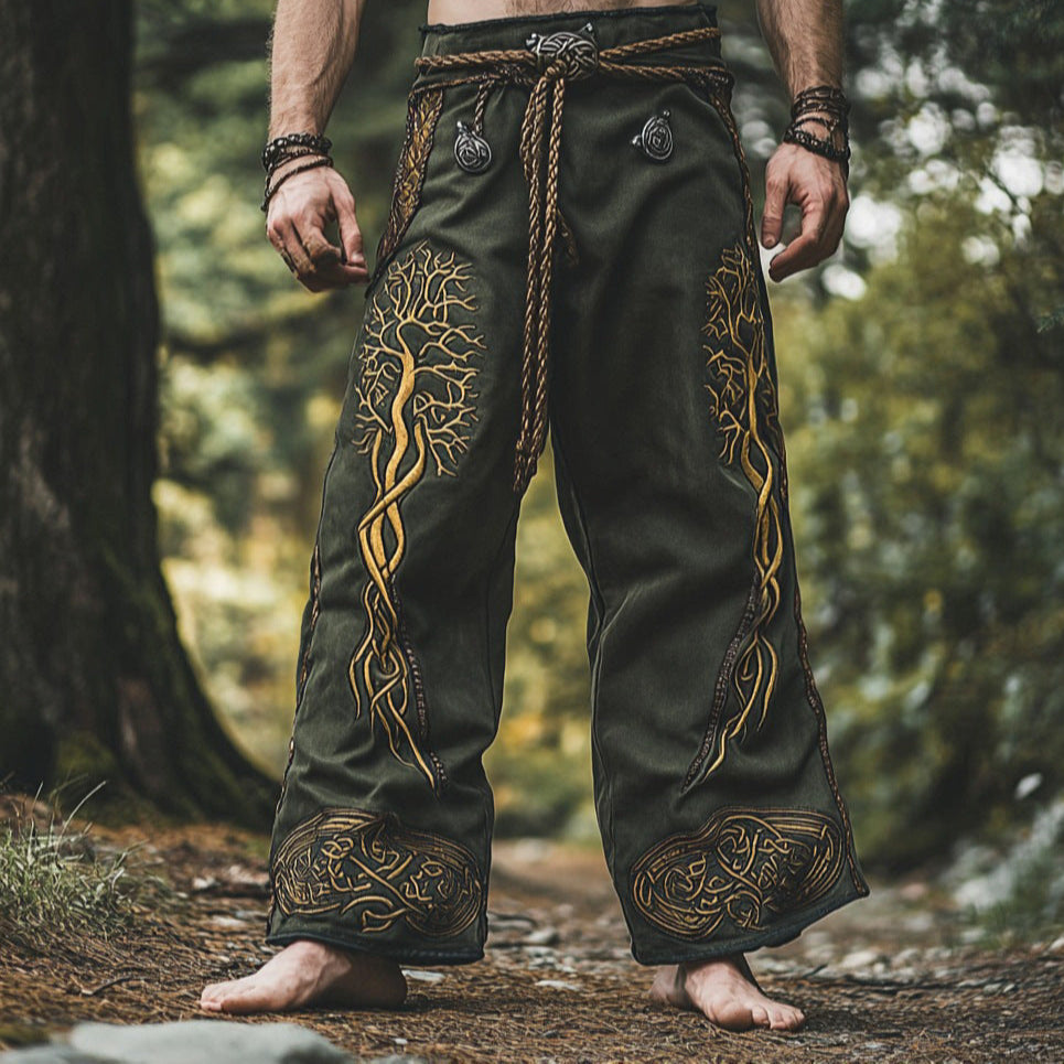 Person wearing dark green pants with gold embroidery in a forest setting