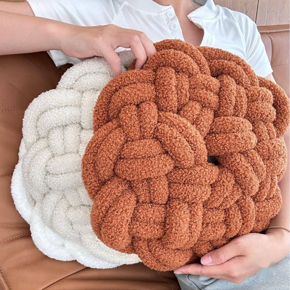 Two braided textured cushions, one white and one brown, held by a person on a leather surface.