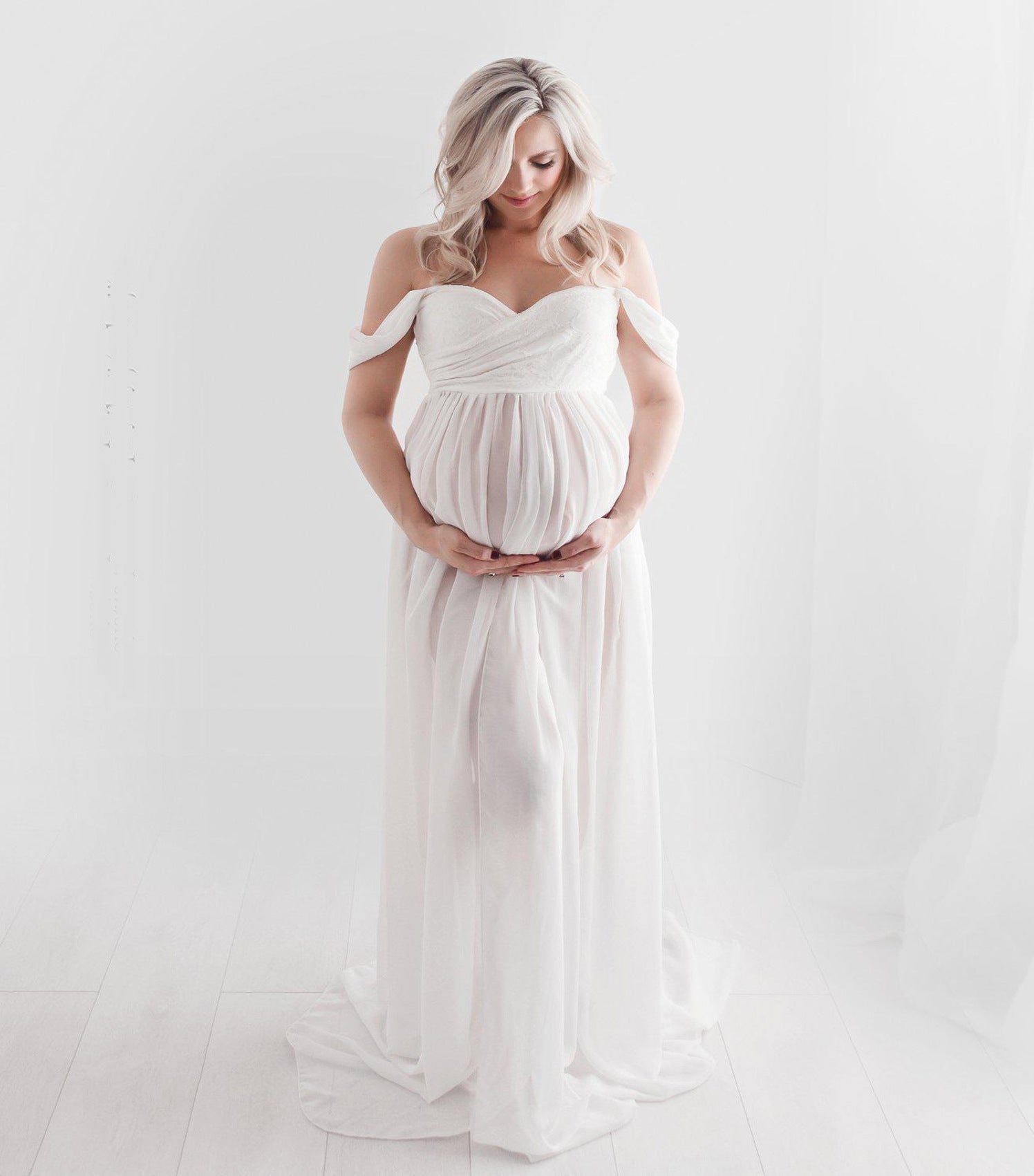 Pregnant woman in a flowing white dress against a plain background