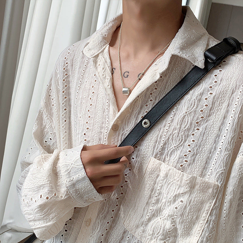 Person wearing a white lace shirt with a black strap over shoulder, holding a phone.