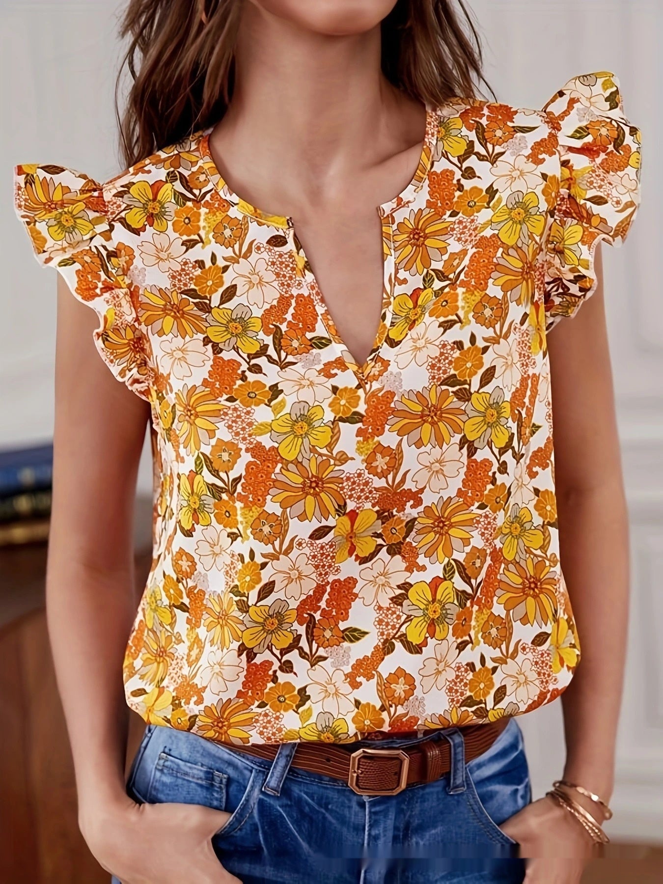 Woman wearing a floral blouse with ruffled sleeves and denim shorts.