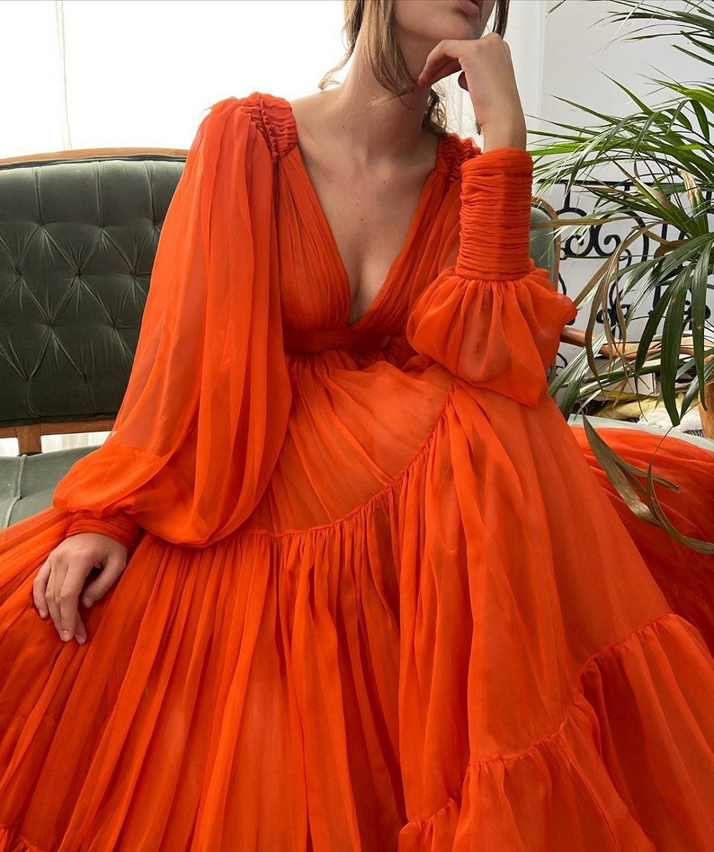 Woman wearing an orange dress with long sleeves and a deep neckline, sitting on a green couch.