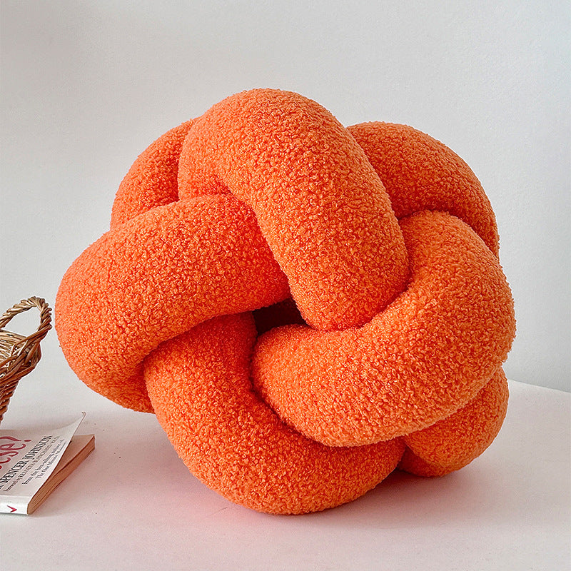 Orange knot-shaped pillow on a light surface with a neutral background