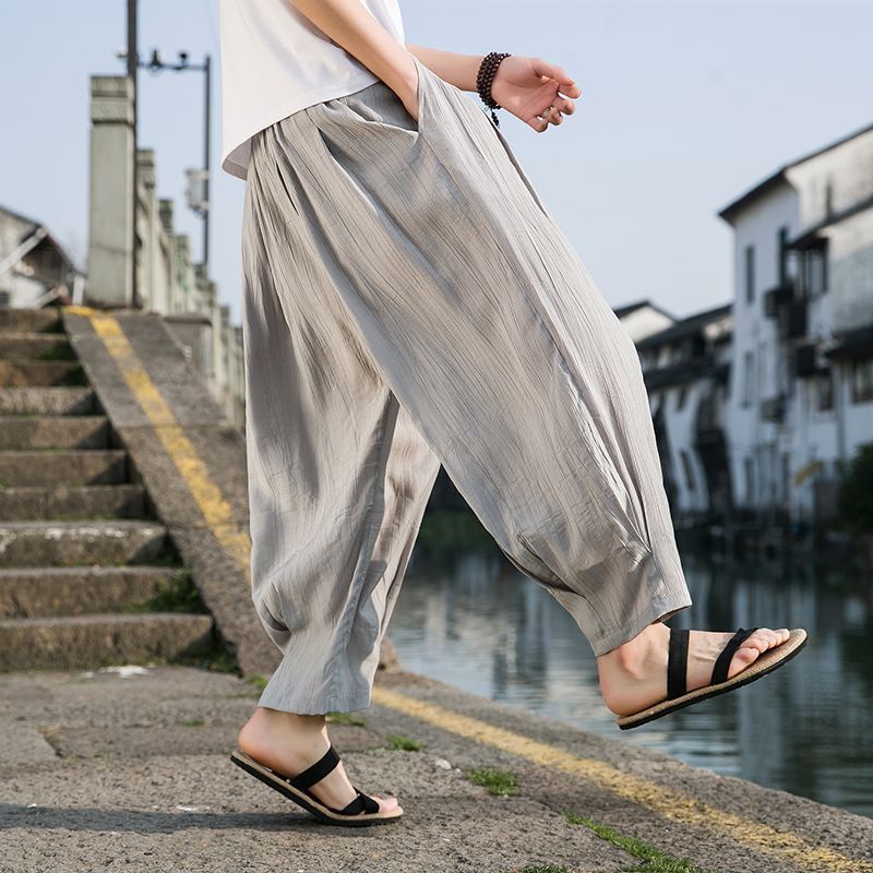 Person wearing light gray wide-leg pants and black sandals by a waterfront with steps and buildings in the background.