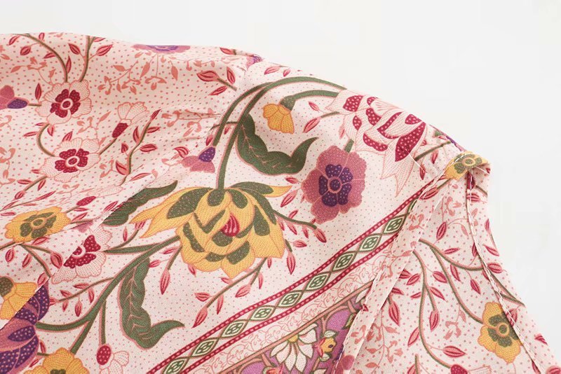 Close-up of a floral patterned fabric with pink, yellow, and green colors on a white background.