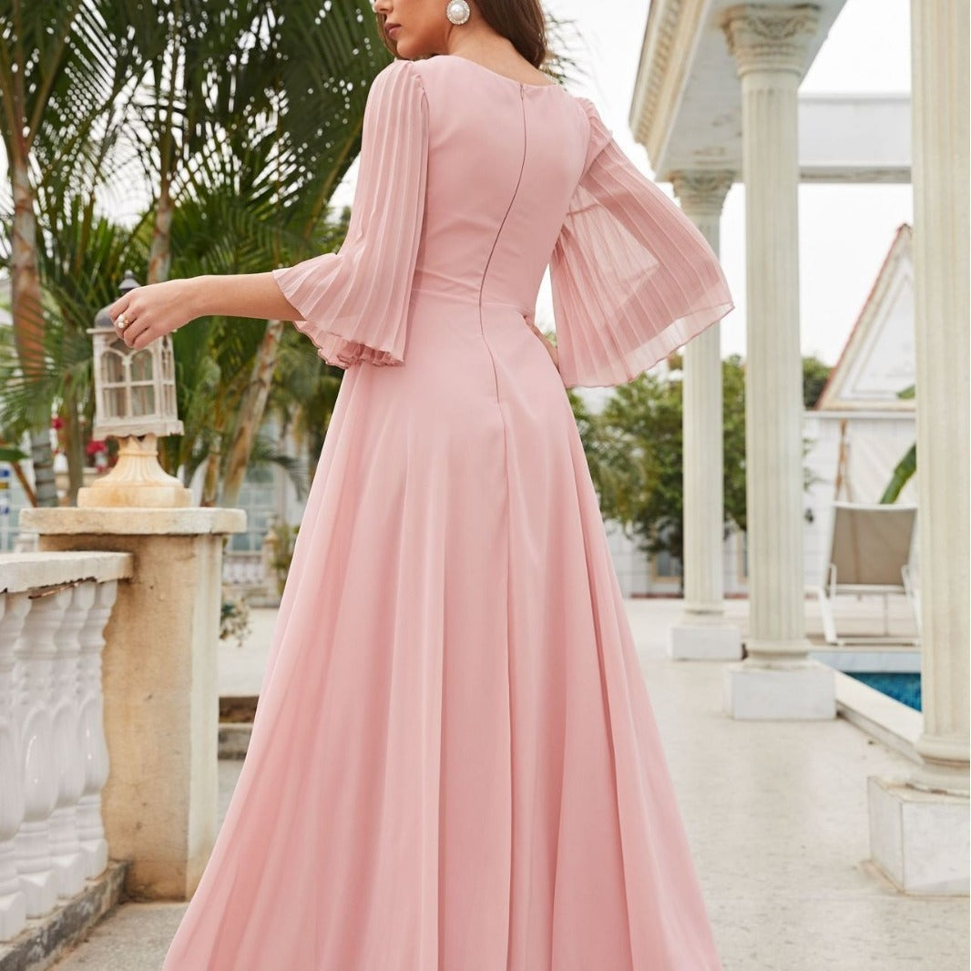 Woman wearing a pink dress with bell sleeves in an outdoor setting.