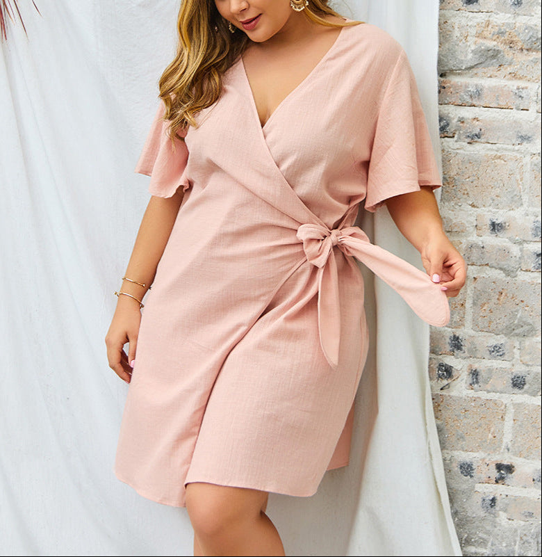 Woman wearing a pink wrap dress against a stone wall.