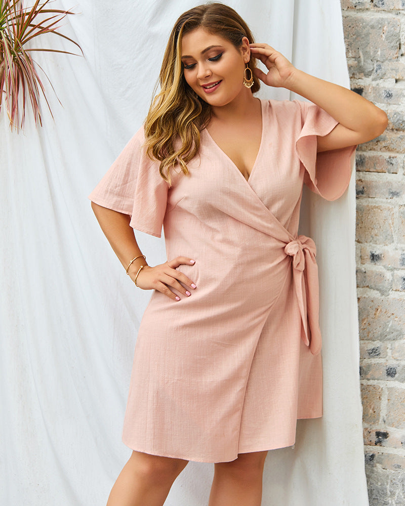 Woman wearing a pink dress with a white curtain and brick wall background