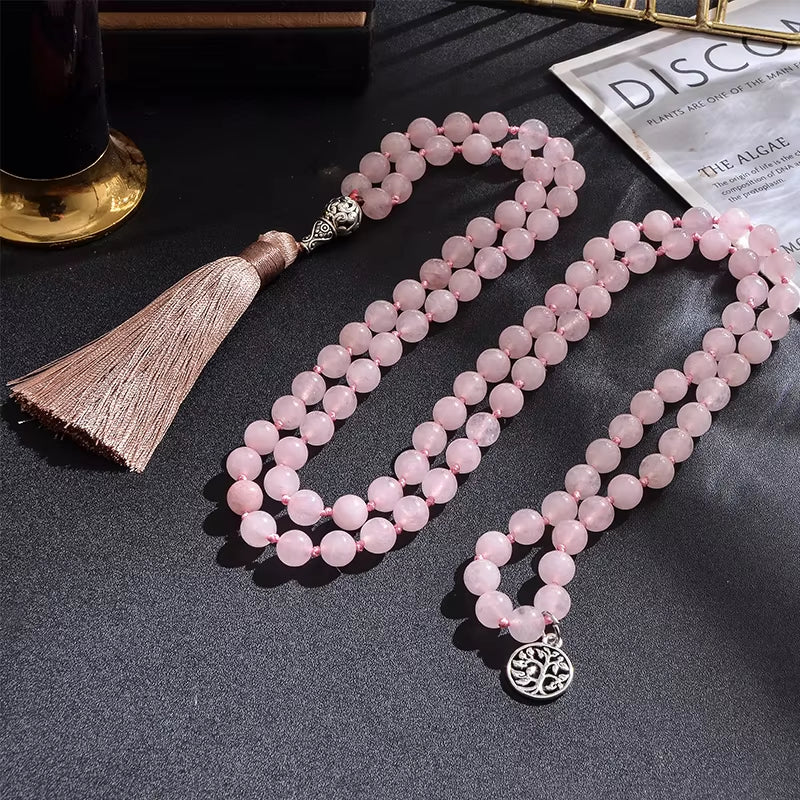 Pink beaded necklace with tassel and silver pendant on a dark surface