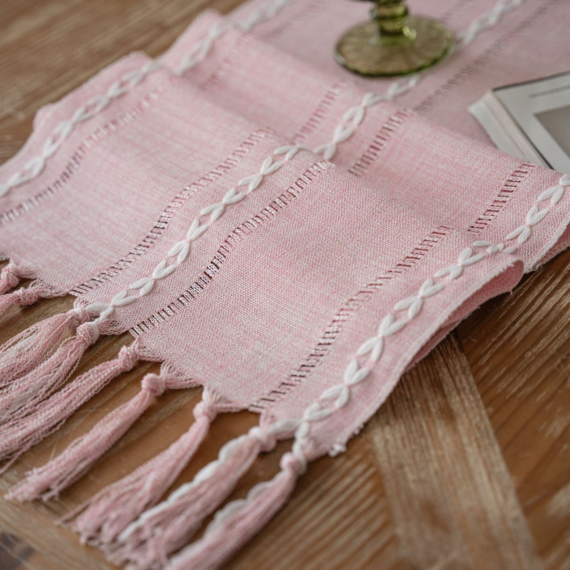 Pink cloth with white embroidery and tassels on a wooden surface
