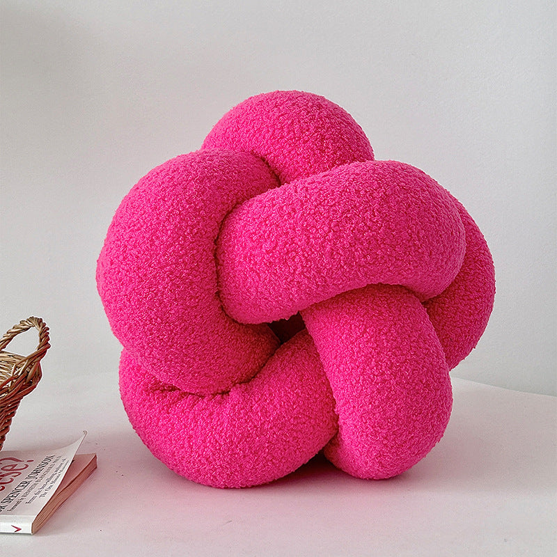 Pink knot-shaped pillow on a white surface with a light gray background