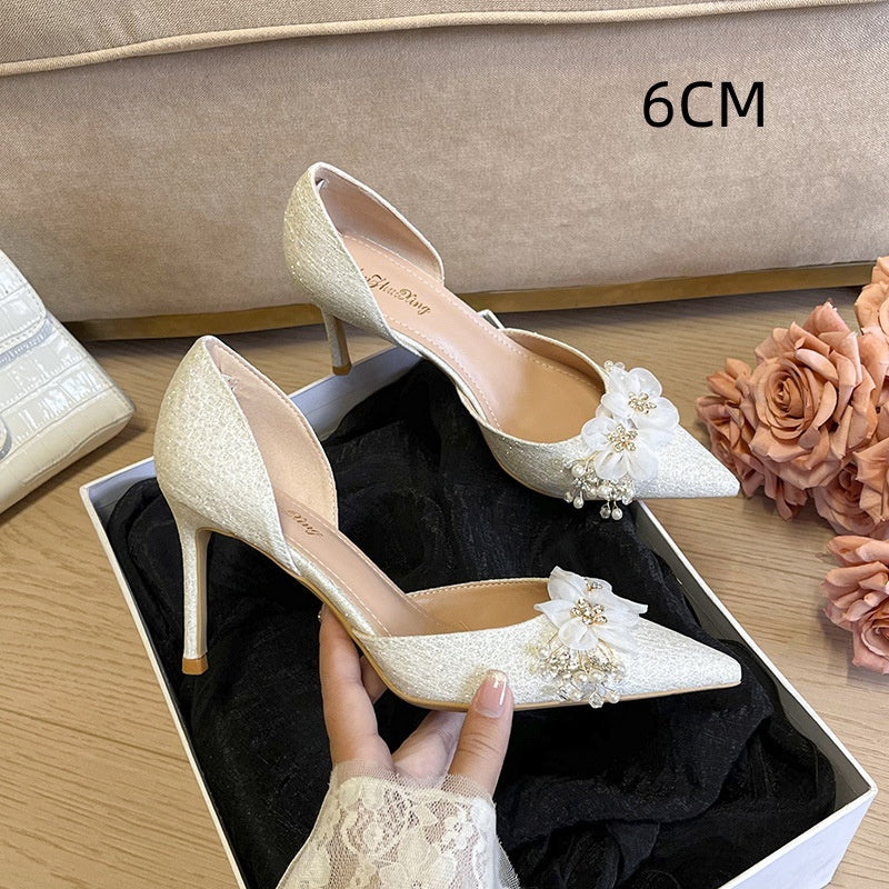 Beige high-heeled shoes with floral decorations in a box on a wooden surface.